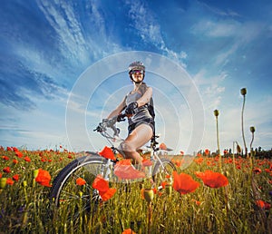 Young woman riding a bicycle on a blooming poppy meadow