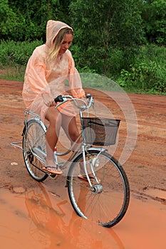 Young woman riding bicycle in tropical summer rain
