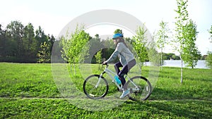 Young woman riding a bike through the park on the background of a lake or river.