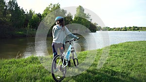 Young woman riding a bike through the park on the background of a lake or river.