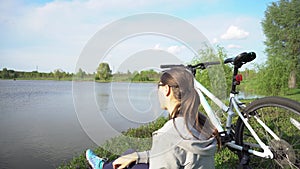 Young woman riding a bike through the park on the background of a lake or river.
