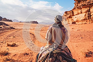 Young woman riding camel in desert. It\'s quite cold so she is wearing traditional Bedouin coat - bisht - and head scarf, photo