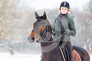 Young woman riding her bay horse on winter field