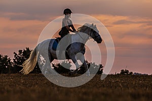 A young woman riding a horse during dusk