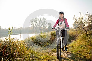 Young woman riding mountain bike along the footpath on the river banks