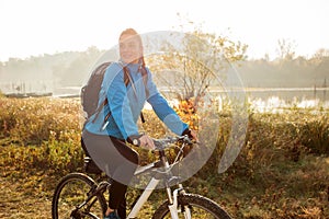 Young woman riding mountain bike on a footpath along the lake shore in early morning sunlight