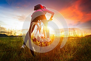Young woman riding mountain bike on the meadow at sunset
