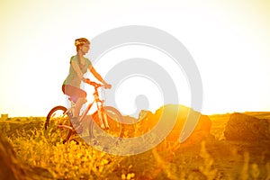 Young Woman Riding Mountain Bike on the Summer Rocky Trail at Beautiful Sunset. Travel, Sports and Adventure Concept.