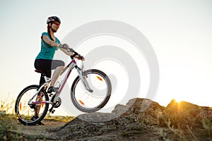 Young Woman Riding Mountain Bike on the Summer Rocky Trail at Beautiful Sunset. Travel, Sports and Adventure Concept.