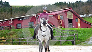 Young woman riding a white horse in a calm equestrian center