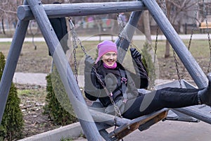 A young woman is riding on a wooden swing smiling on a sunny autumn day