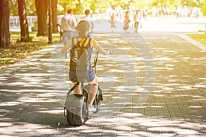 A young woman riding zero-emission eco electric scooter bike in a city park.