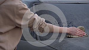 A young woman rinses off the inscription on the machine with a rag: & x22;Please wash me.& x22; Girl washes a dirty car. Prank