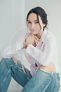 Young woman in ripped jeans and shirt poses sitting