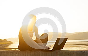 Young woman by the river in susnset with laptop