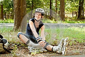 Young woman on roller skates sitting holding foot