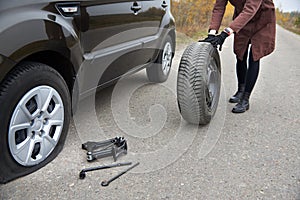 A young woman rolls spare tire near her car with a flat tire