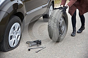 A young woman rolls spare tire near her car with a flat tire