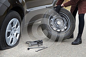 A young woman rolls spare tire near her car with a flat tire