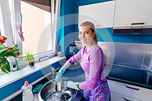Young woman in rubber gloves washing dishes