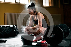 Young woman rubs hands in chalk before lifting barbell