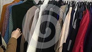 A young woman rummages through a rack of secondhand sweaters, thrift shop