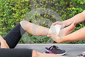 Young woman runner ankle being applied bandage by man in park. i