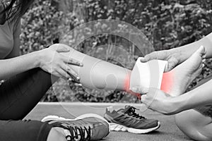 Young woman runner ankle being applied bandage by man in park. i