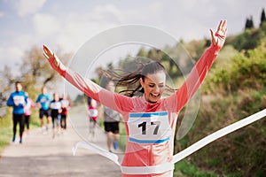 Young woman runner crossing finish line in a race competition in nature.