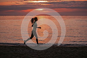 Young woman runner goes in for sports on the seashore at sunrise. Cardio load, fitness for fit