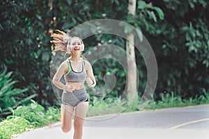 Young woman runner listening music on headphones while running on road in the morning