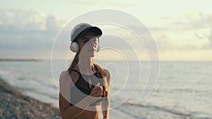 A young woman runner is listening to music in earphones and training by a sea. Close up of fitness girl is jogging