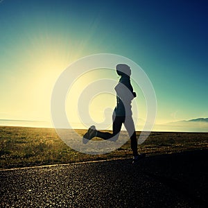 Young woman runner running on sunrise seaside road