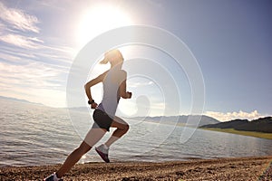 Young woman runner running on sunrise seaside road