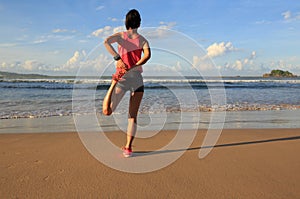 young woman runner stretching legs before running on sunrise seaside