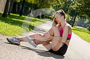 Young woman runner touching foot in pain outdoors