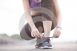 young woman runner tying shoelaces before jogging standing on footpath.