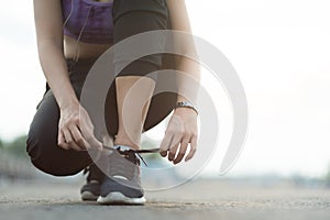 young woman runner tying shoelaces before jogging standing on footpath.