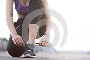 young woman runner tying shoelaces before jogging standing on footpath.