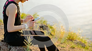 Young Woman Runner Using Smartphone and Listening to Music at Sunset on the Mountain Trail. Sports Concept