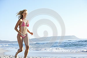 Young Woman Running Along Sandy Beach On Holiday Wearing Bikini