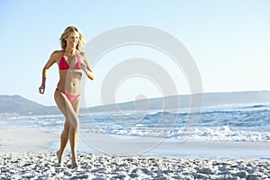 Young Woman Running Along Sandy Beach On Holiday Wearing Bikini