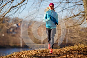 Young woman running in autumn park at sunny day