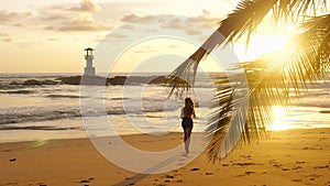 Young woman running barefoot on sea beach with sunset ocean background. Female athlete silhouette exercising cardio