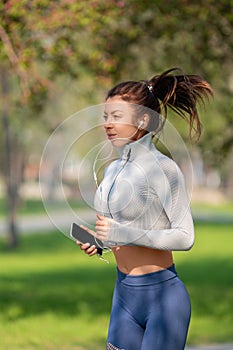 Young woman running in the city park in early morning. Attractive looking woman keeping fit and healthy. Vertical photo.