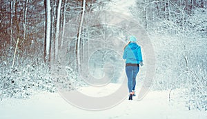 Young woman running down a path in the winter woods through snow