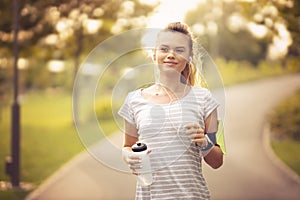 Young woman running in park and listening to music with headphones - Beautiful blonde and fit girl jogging alone outdoor in early