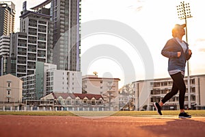 Young woman is running on racetrack at sunset, building behind