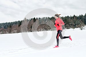 Young woman running on snow in winter mountains wearing warm clothing gloves in snowy weather