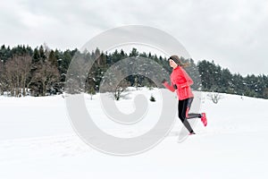 Young woman running on snow in winter mountains wearing warm clothing gloves in snowy weather